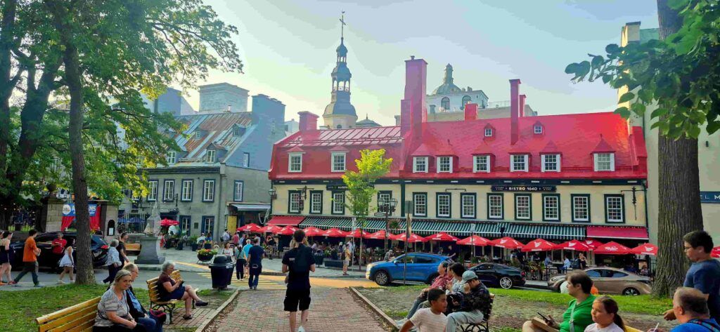 Personas sentadas en un parque de la parte alta de Quebec, Canadá, con un impresionante edificio rojo al fondo