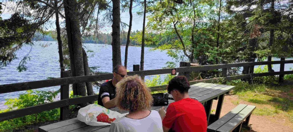 Tres personas comiendo en un merendero junto al Lago Wapizagonke del Parque La Mauricie en Canadá