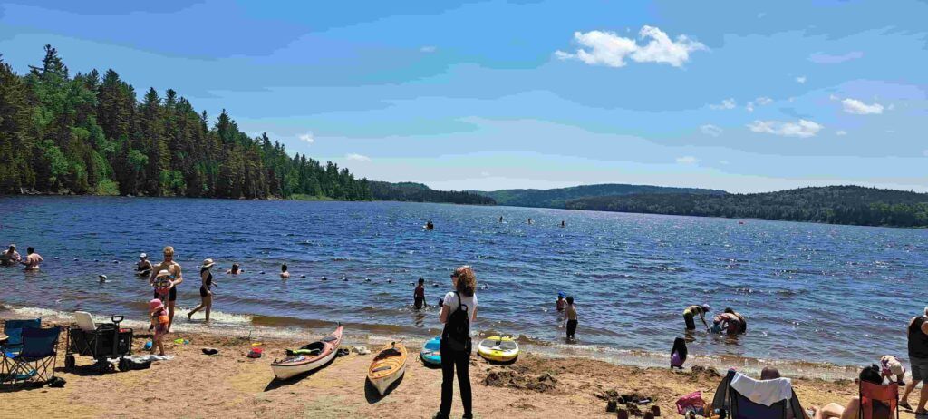 Mujer contemplando la Playa Édouard llena de gente en un día de verano en el Parque La Mauricie en Canadá