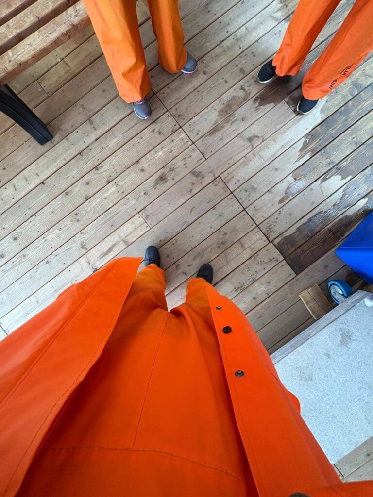 Piernas de tres personas vestidas con el traje color naranja de las excursiones para avistar ballenas en Tadoussac, Canadá