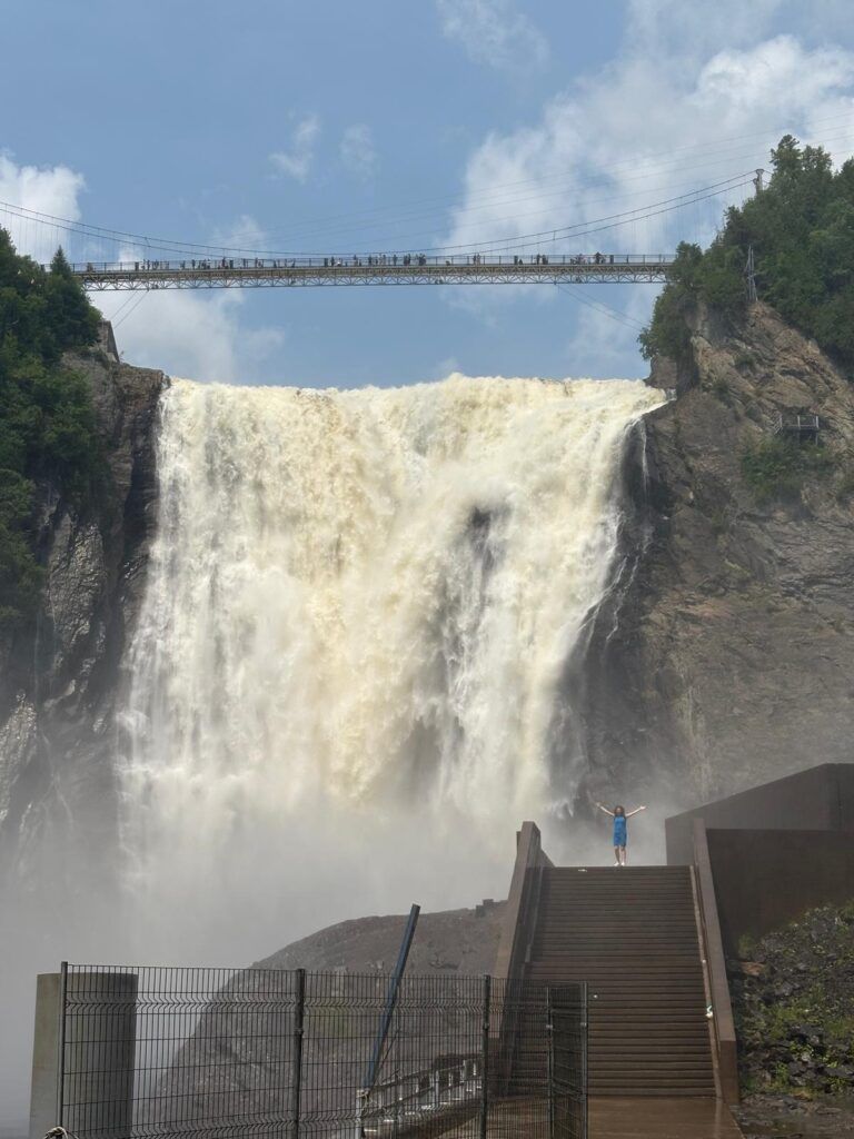 Persona  a lo lejos con los brazos abiertos, mojándose, en la base de la Cascada de Montmorency, en Canadá
