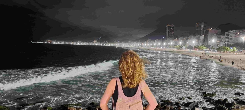 Mujer de espaldas admirando el mar y la playa de Copacabana durante la noche, desde el Morro do Leme
