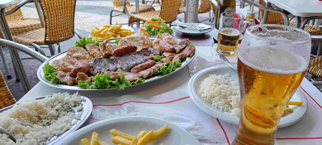 Mesa de un restaurante en Copacabana con  cervezas, una bandeja con churrasco y platos de arroz y patatas fritas