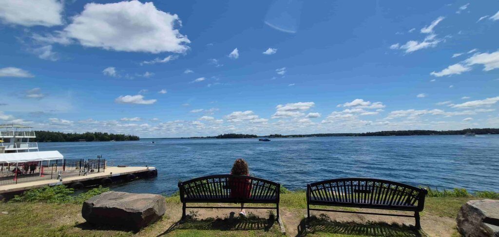 Mujer de espaldas sentada en un banco con vistas al Río San Lorenzo a su paso por Rockport, Canadá