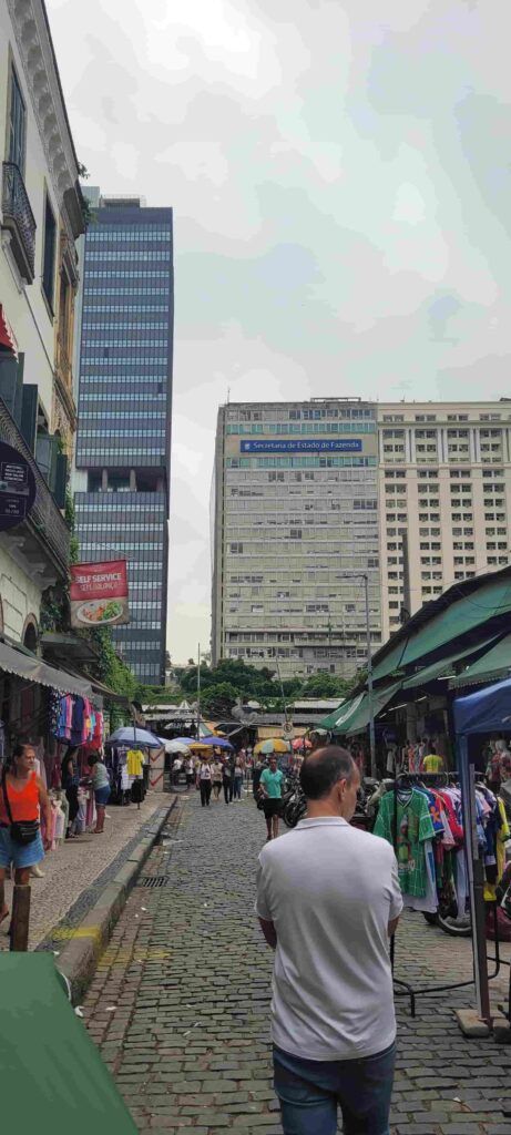 Hombre de espaldas en una calle del centro de Río de Janeiro con gente paseando y con comercios de ropa en la misma calle