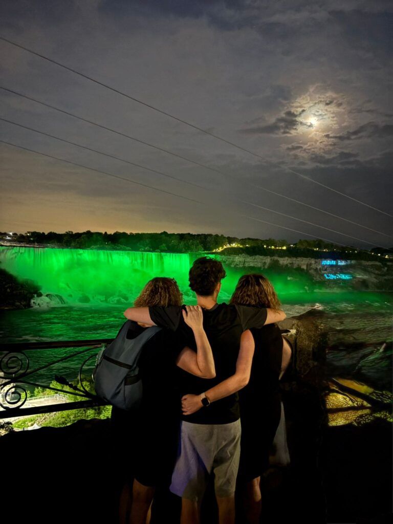 Familia de espaldas abrazada, contemplando las Cataratas del Niágara iluminadas, en una noche de verano