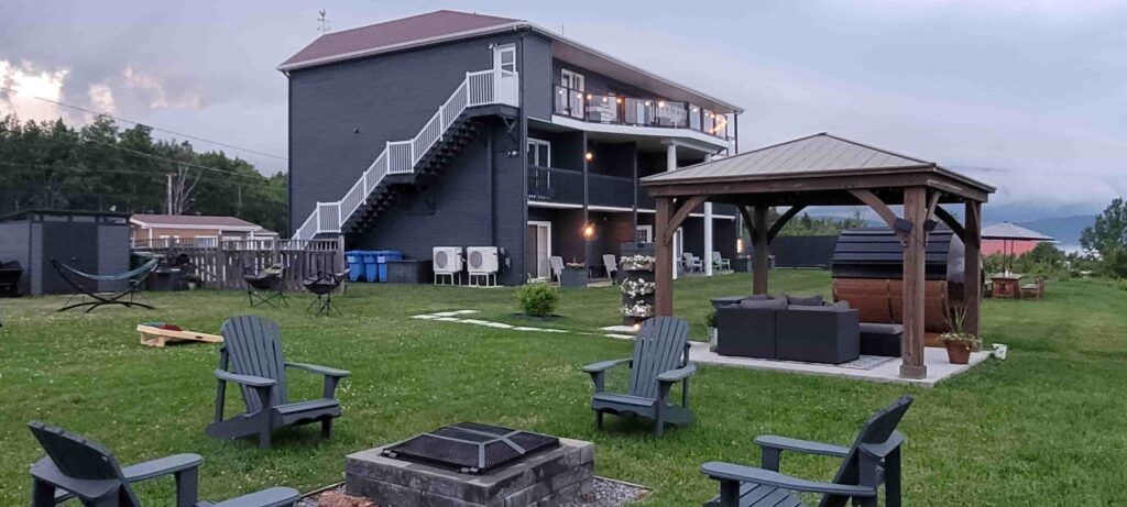 Edificio y jardín del Motel Horizon, en Saint-Siméon, Canadá, con butacas de madera alrededor de un brasero de leña